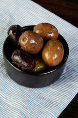 Black and green olives in wooden plate on wooden background. Salted olives. International cuisine. Harvesting.