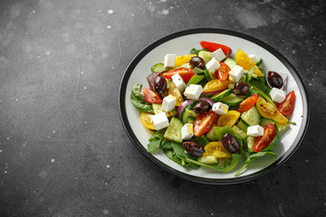 Fototapeta na wymiar Fresh Greek salad with cucumber, cherry tomato, lettuce, red onion, feta cheese and black olives. Healthy food