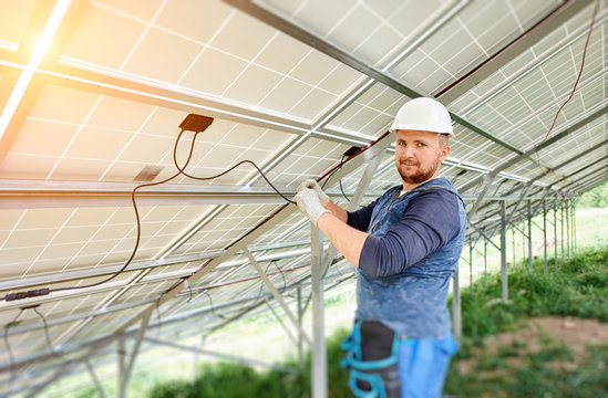 Installing and wiring of stand-alone solar photo voltaic panel system. Close-up of young electrician in hard-hat connecting electrical cables inside the solar modules. Alternative energy concept.