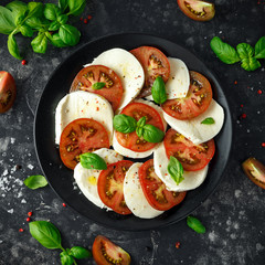Caprese salad with tomatoes, mozzarella cheese and fresh basil leaves in a black plate. Italian food.