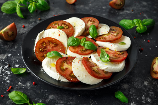 Caprese salad with tomatoes, mozzarella cheese and fresh basil leaves in a black plate. Italian food.