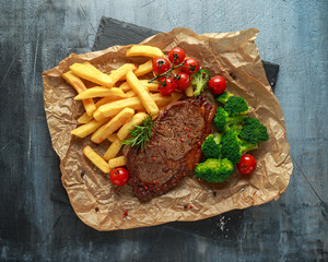 Grilled sirloin steak with potato fries, broccoli and cherry tomatoes on crumpled paper