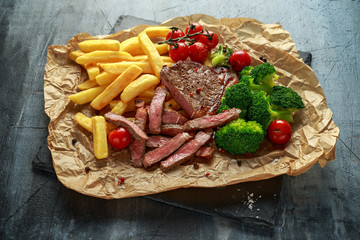Grilled sirloin steak with potato fries, broccoli and cherry tomatoes on crumpled paper