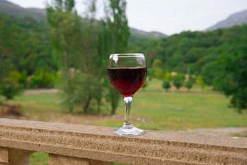 Outdoor picnic setting with wine or glass of wine on balcony with green field and mountains on background