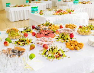 Served tables at the Banquet. Desserts, fruit and pastries on the buffet. Glassware and mineral water bottles. Roses in a jug. Catering.