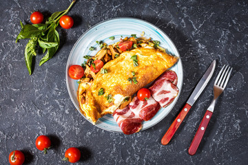 Omelet with tomatoes, mushrooms and bacon. Breakfast on stone background. Top view.
