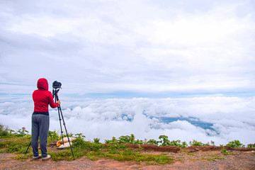 Photographer taking Thailand travel nature photography. Woman photographer shooting with tripod and DSLR camera in sunset with beautiful landscape in background.