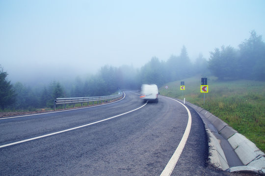 Photo of foggy road crossing the mountains with motion blurred van driving on it
