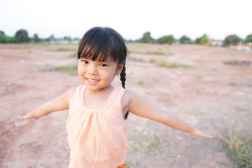 Asian children cheerful or kid girl poor smile show two hand and play running for happy fun because come back home at country and wear traditional top or sleeveless shirt on arid soil for agriculture