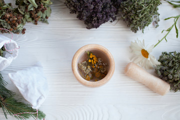 Bunches of healing herbs and mortar on white wooden plank. Herbal medicine. Top view, flat lay....