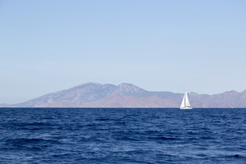 Sailing boat cruising in blue waters, mountains and shore seeing in background
