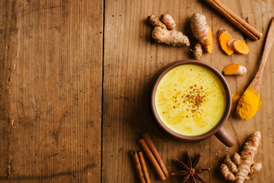 Hot turmeric milk with spices on wooden table