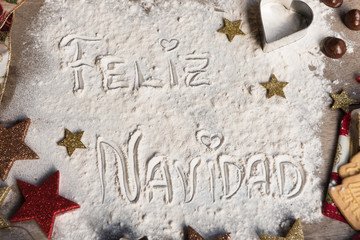 Feliz Navidad, spanish text made with flour, surrounded by Christmas decorations.