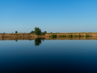 River landscape. Beautiful view of the full-flowing river from the high steep Bank, overgrown with grass. The blue surface of the water, cloudy sky and green grass on the opposite Bank of the river