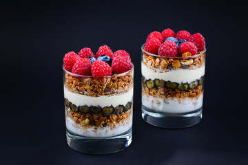 Healthy blueberry and raspberry parfait in a glass on a black background. Two portions. Space for text or design.