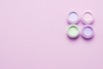 Cosmetics. Makeup. Jars with  crumbly bright shadows, glitter. Pink, green, lilac colors on lilac background. Closeup. Space for text or design.