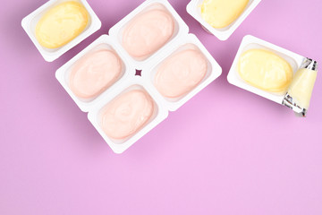 Plastic cup with tasty yogurt on lilac background. Top view. Space for text or design.