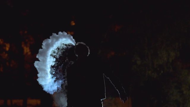 The man smoking an electric cigarette on the dark background. slow motion