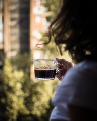 A girl holding cup of black coffee, blurred background..