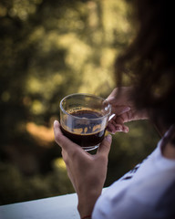 A girl holding cup of black coffee, blurred background..