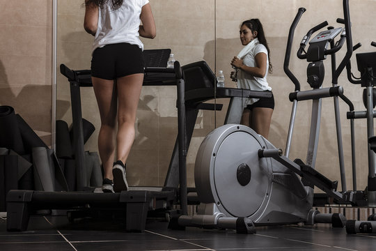 Mujer joven entrenado en la cinta de correr en el gimnasio con camiseta blanca y pantal&oacute;n corto negro