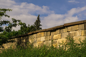 Fototapeta na wymiar An old stone wall below a cloudy summer sky