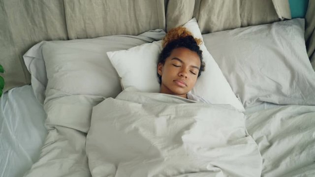 Young African American woman sleeping in comfortable bed under warm blanket having rest on beautiful linen. Comfort, resting people and bedroom concept.