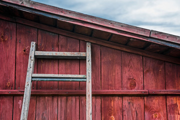 The ladder rests on the wall of a wooden red barn