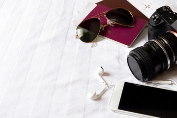 Top view of traveler accessories on the bed with digital camera, cellphone, sunglasses and passport.