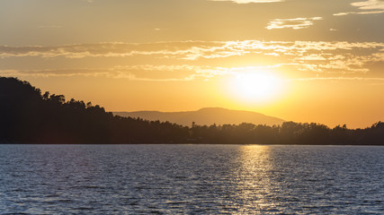 Sunset above the lake or sea. Silhouettes of horizon under the sun.