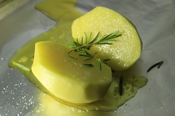 Close up of a potato with rosemary and oil on it, ready to be cooked