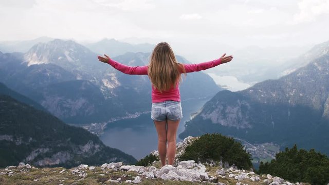 Back view of young woman rise her hands enjoying amazing view of lake in mountains