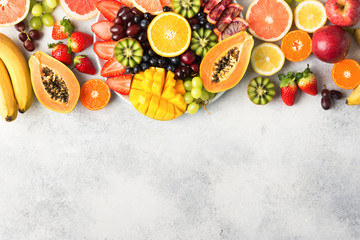 Assortment of raw fruits berries, mango, oranges, kiwi strawberries, blueberries grapefruit grapes, bananas apples on the white plate, on the off white table, top view, copy space