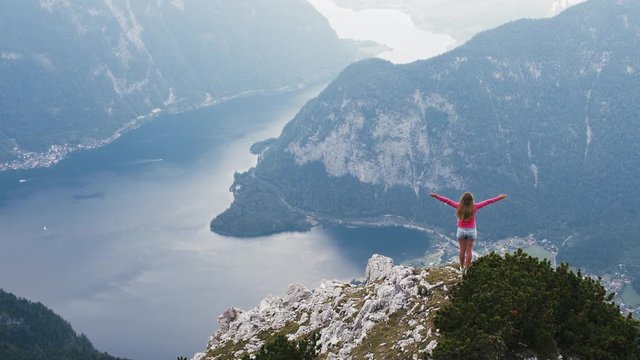 Back view of young woman rise her hands enjoying amazing view of lake in mountains