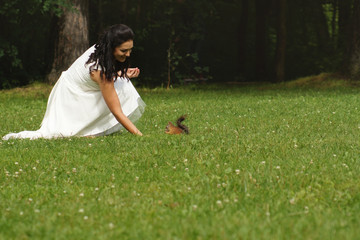 Beautiful brunette in white dress squatting in park and feeding squirrel