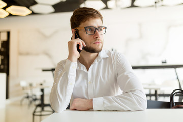 Pensive young businessman in cafe using phone