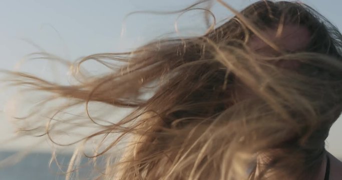 Slow motion closeup portrait of young girl standing on a beach and wind blows her hair