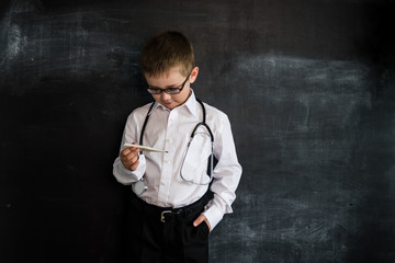 Young boy's standing near blackboard checking thermometer. Young doctor. Creative design concept for 2019 calendar.