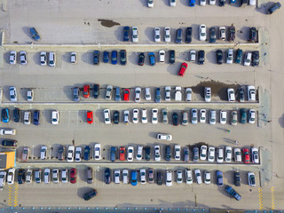 Aerial view of a large number of cars of different brands and colors standing in a parking lot near the shopping center in a chaotic manner. Parking divided by white dividing strips and sidewalks