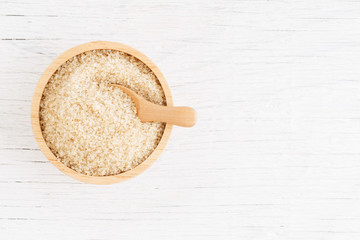 brown sugar and wood spoon in brown bowl on white wooden table, top view and copy space