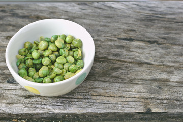 Green peas In white cup on old wooden floor.