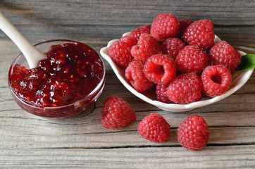Fresh raspberry jam in a glass bowl and freshly picked raspberries on old wooden background.
Selective focus.
