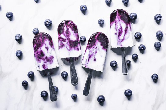 Blueberry coconut milk swirl popsicles with lime on marble background