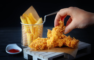 Hand grabs crispy kentucky fried chicken french fries and tomato on black wooden table