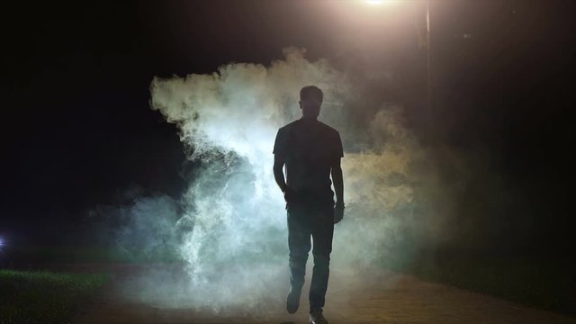 The man walking near the cloud of smoke on the dark background, slow motion