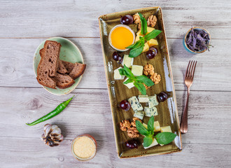 Cheese platter garnished with honey, walnuts, grapes, bread, mint and glass of wine over wooden background