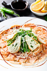 Fish carpaccio with arugula, crackers and cheese parmesan on dark wooden background. Delicious appetizers