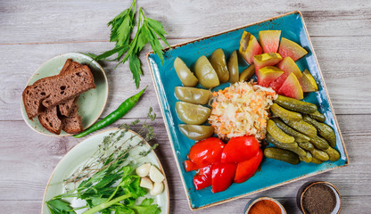 Assorted pickled vegetables - Sauerkraut cabbage, watermelon, peppers, cucumbers, tomatoes and herbs on light wooden background