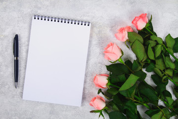 Bouquet of pink roses and a blank notebook with pen, pencil on a light background.