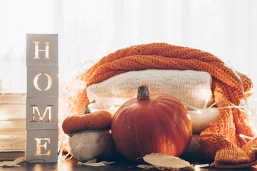 Background with warm sweaters and the inscription HOME. Pile of knitted clothes with leaves, pumpkins. Coziness. Autumn concept